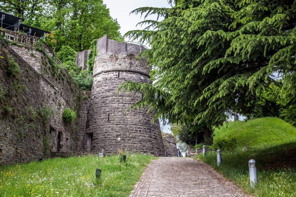Ruiny zamku na wzgórzu San Vigilio kryją się wśród zieleni wysoko nad Górnym Miastem w Bergamo.